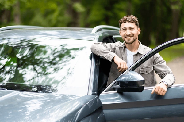 Image of a genuinely smiling driver next to their car